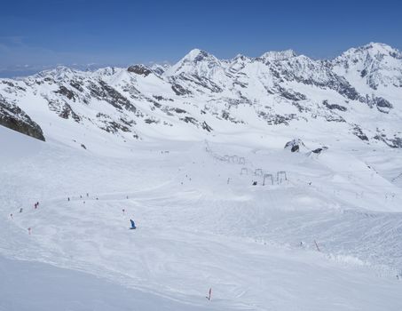 Winter landscape with snow covered mountain slopes and pistes with skiers enjoying spring sunny day at ski resort Stubai Gletscher, Stubaital, Tyrol, Austrian Alps.