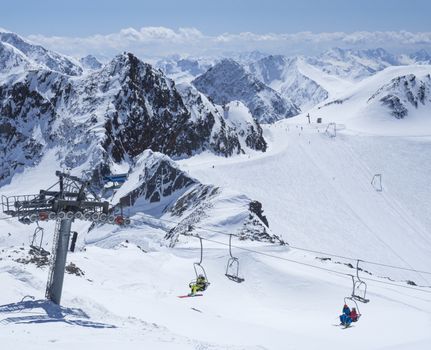 Scenic view from top of Wildspitze on winter landscape with snow covered mountain slopes and pistes and skiers on chair lift at Stubai Gletscher ski resort at spring sunny day. Blue sky background. Stubaital, Tyrol, Austrian Alps