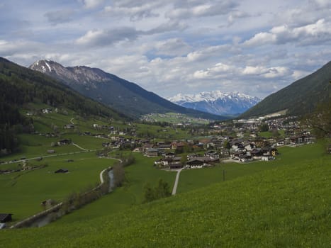 Idyllic spring mountain rural landscape. View over Stubaital or Stubai Valley near Innsbruck, Austria with village Neder and Neustift im Stubaital, green meadow, snow covered alpen mountain peaks.
