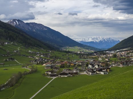 Idyllic spring mountain rural landscape. View over Stubaital or Stubai Valley near Innsbruck, Austria with village Neder and Neustift im Stubaital, green meadow, snow covered alpen mountain peaks.
