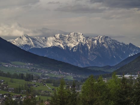 Spring mountain rural landscape. View over Stubaital Stubai Valley near Innsbruck, Austria with village Neder, green meadow, forest, snow covered alpen mountain peaks, evening dramatic clouds and light.