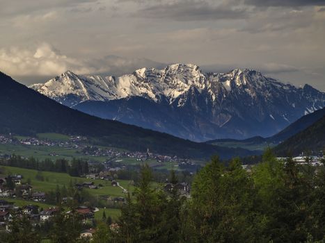 Spring mountain rural landscape. View over Stubaital Stubai Valley near Innsbruck, Austria with village Neder, green meadow, forest, snow covered alpen mountain peaks, evening dramatic clouds and light.