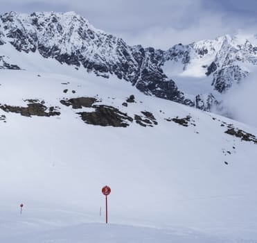 Winter landscape with empty red piste sign, snow covered mountain slopes, spring sunny day at ski resort Stubai Gletscher, Stubaital, Tyrol, Austrian Alps
