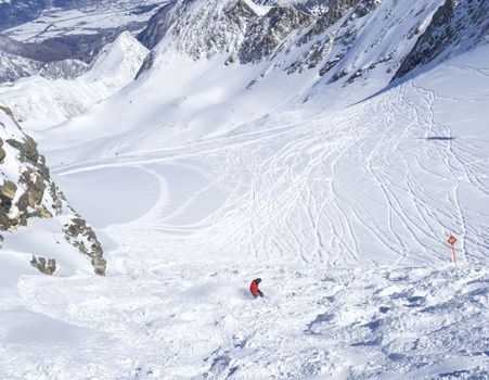 Free ride piste with snowboarder in red clothes skiing downhill on snow covered slopes from the top of Kitzsteinhorn mountain at Kaprun ski resort, National Park Hohe Tauern, Austrian Alps, Europe. Sunny winter day