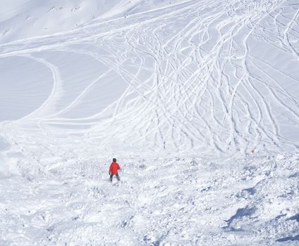 Free ride piste with skier in red clothes skiing downhill on snow covered slopes from the top of Kitzsteinhorn mountain at Kaprun ski resort, National Park Hohe Tauern, Austrian Alps, Europe. Sunny winter day
