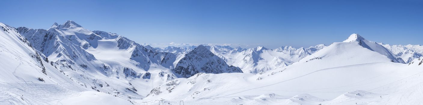Panoramic landscape view from top of Schaufelspitze on winter landscape with snow covered mountain slopes and pistes at Stubai Gletscher ski resort at spring sunny day. Blue sky background. Stubaital, Tyrol, Austrian Alps.