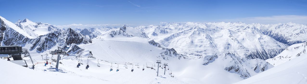 Panoramic landscape view from top of Schaufelspitze on winter landscape with snow covered mountain slopes and pistes at Stubai Gletscher ski resort at spring sunny day. Blue sky background. Stubaital, Tyrol, Austrian Alps.
