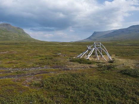 Beautiful northern landscape with Kungsleden hiking trail path and remains of sami hut. Green bushes, rocky mountains and dramatic clouds. Summer sunny day.