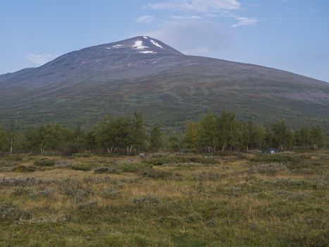 Colorful mountain Sanjartjakka with small tent and Beautiful wild Lapland nature landscape with birch tree forest. Blue sky background.