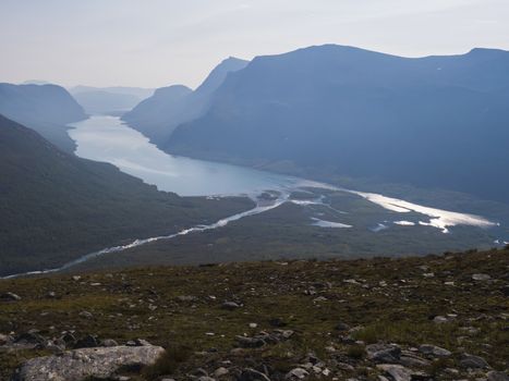 Aerial view from mountain Sanjartjakka on wild Lapland landscape with Tjaktjajakka river, Kaitumjaure lake, birch tree forest and mountains. Northern Sweden summer. Blue sky background, backlight.