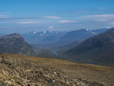 Aerial view from mountain Sanjartjakka on wild Lapland landscape with Tjaktjajakka river valley, and snow capped mountains. Northern Sweden summer. Blue sky background.