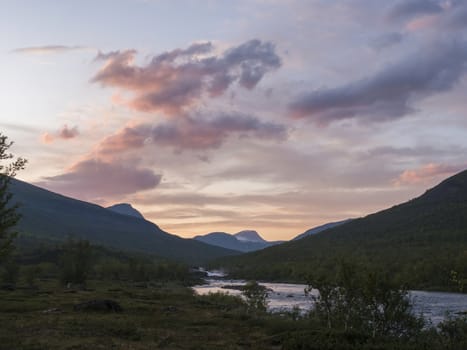 Wild Tjaktjajakka river and Kaitumjaure lake with waterfall cascade and mountains. Lapland nature landscape in summer, sunset pink clouds.