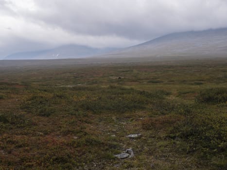 Lapland highlands mountains with autumn colored bushes and heath in mist and clouds.