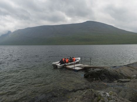 group of tourist hikers on motor boat at pier prepar to crossing Teusajaure lake at Kungsleden hiking trail. Lapland mountains nature landscape in summer, moody sky