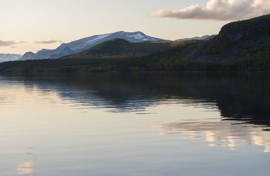 Beautiful beautiful blue orange sunset over the lake Lulealven in Saltoluokta in Sweden Lapland. Reflection of mountains, clouds and sky in clear the water. Minimalist, copy space.