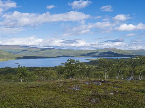 Lapland landscape with beautiful river Lulealven, snow capped mountain, birch tree and footpath of Kungsleden hiking trail near Saltoluokta, north of Sweden wild nature. Summer blue sky.