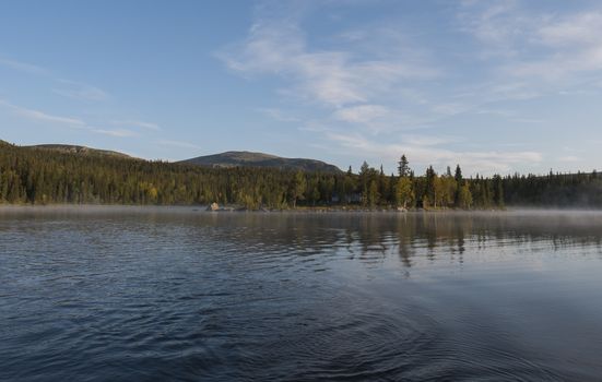 Beautiful morning over lake Sjabatjakjaure with view on Parte Fjallstuga STF mountain cabin, green hills and birch trees. Sweden Lapland at the Kungsleden Trail.