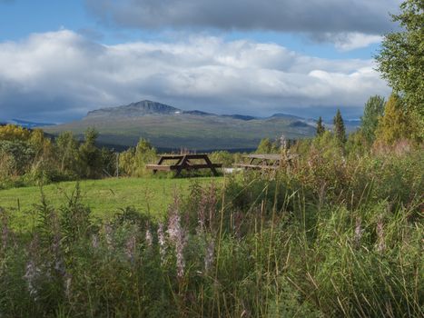 Wooden picninc tables with view on beautiful landscape of Sarek mountains in Kvikkjokk in Swedish Lapland. Summer sunny day, golden hour, dramatic clouds.