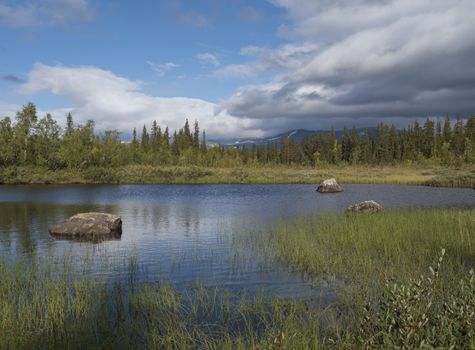 Beautiful northern landscape with river basin of Kamajokk, boulders, mountain peaks and spruce tree forest in Kvikkjokk in Swedish Lapland. Summer sunny day, dramatic clouds.