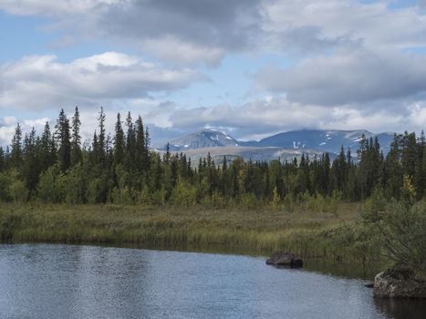 Beautiful northern landscape with river basin of Kamajokk, boulders, mountain peaks and spruce tree forest in Kvikkjokk in Swedish Lapland. Summer sunny day, dramatic clouds.