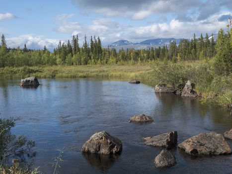 Beautiful northern landscape with river basin of Kamajokk, boulders, mountain peaks and spruce tree forest in Kvikkjokk in Swedish Lapland. Summer sunny day, dramatic clouds.