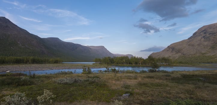 Wide panoramatic Lapland nature landscape with cofluence of wild Tjaktjajakka river and Kaitumjaure lake with small birch tree forest island and mountains. Summer at North sweden wilderness