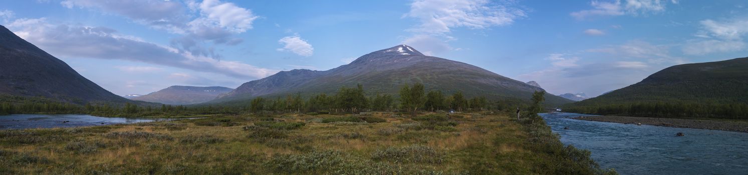 Wide panoramatic Lapland nature landscape with angler fisherman and small tent at blue Tjaktjajakka river, Kaitumjaure, birch tree forest and mountain Sanjartjakka. Summer at North sweden wilderness