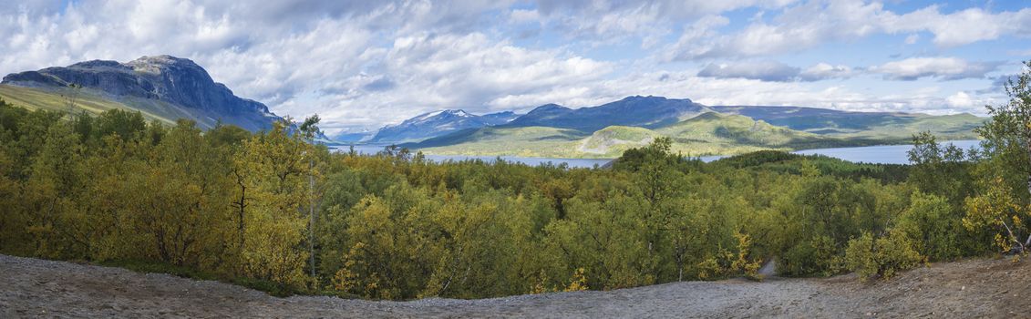 Panoramic landscape with beautiful river Lulealven, snow capped mountain and yellow birch tree. Kungsleden hiking trail near Saltoluokta, north of Sweden, Lapland wild nature. Early autumn blue sky.