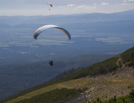 Two paragliders fly over a mountain valley on a sunny summer day. Kiting in blue and orange kite in tatra mountains Slovakia at summer sunny day.