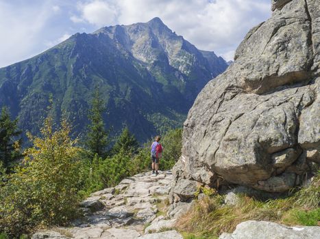 Senior tourist woman hiking at the beautiful nature trail at high tatra mountains in slovakia, summer sunny day.