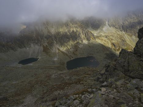 Panorama from Bystra lavka 2300m to the mountain lake Beautiful Capie and Okruhle pleso in Mlynicka dolina and mountain peak Strbsky stit 2381m , slovakian high Tatra mountains. Summer panorama with fog and dramatic light.