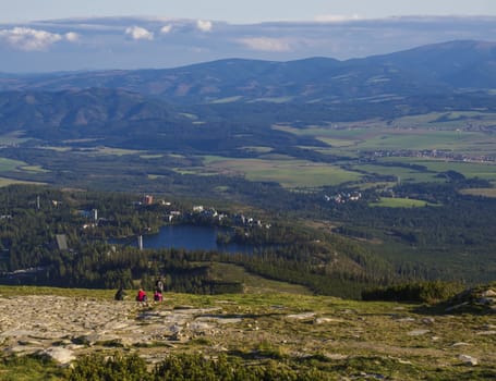 Aerial view on Strbske pleso village and blue mountain lake from chata pod soliskom with forest, hills and group of relaxing tourist watching view, High Tatra mountains, Slovakia, summer, golden hour light