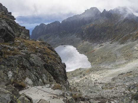 Beautiful Vysne Wahlenbergovo pleso mountain lake in Furkotska dolina view from Bystre sedlo with steep trail with chain in slovakian high Tatra mountains. Summer panoramas lovakian high Tatra mountains, fog and dramatic light.