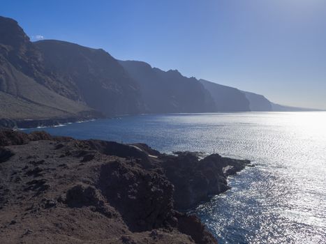 view on hight lava cliffs los gigantes on Punta de Teno cape on west Tenerife canary island with lava rock blue sea and clear summer sky Contre-jour against daylight