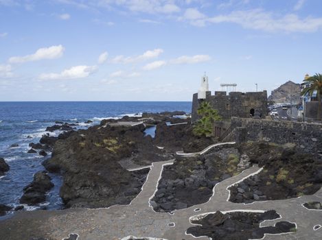 View on village Garachico with sea pools and lava rocks and main road and fortification in Tenerife canary island spain with blue sky white clouds background