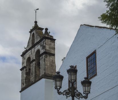 Traditional church stone bell tower and street lamp in Puerto de la cruz, Spain, Canary islands, Tenerife, blue sky white clouds.