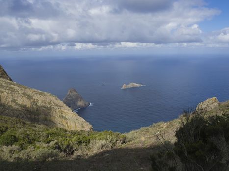 view on rock in the sea El Draguillo with green hills and dramatic blue sky white clouds in anaga mountain, tenerife  canary island spain
