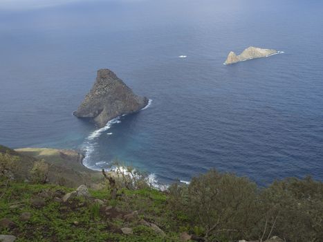 view on rock in the sea El Draguillo with green hills and dramatic blue sky white clouds in anaga mountain, tenerife  canary island spain