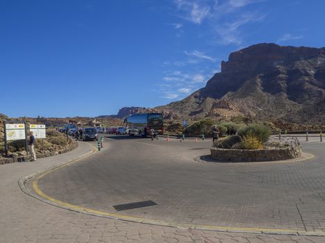 Spain, Canary islands,Tenerife, El Teide national park, December 21, 2017, traffic circle on parking at Roque Cinchado famous pitoresque rock formation Roques de Garcia with group of tourist, bus, parked cars, touristic notice and blue sky background