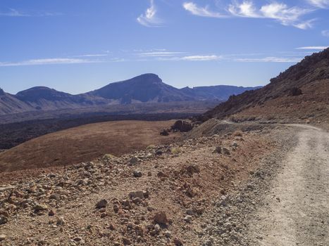 curved footpath road to volcano pico del teide with desert volcanic landscape orange and purple mountain, clear blue sky background