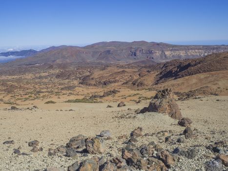 desert volcanic landscape on Tenerife with purple mountains in el teide national nature park with Huevos del Teide (Eggs of Teide) lava balls rocks, clear blue sky background