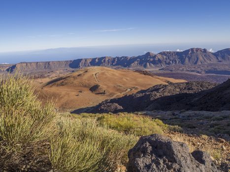 view on montana blanca on tenerife desert volcanic landscape with purple mountains orange sand and dry green bush in el teide national nature park with lava field and rocks on clear blue sky background