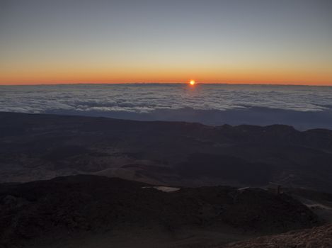 red sunrise sun rising on horizon from white clouds on the top of pico del teide vulcano highest spanish mountain on tenerife canary island