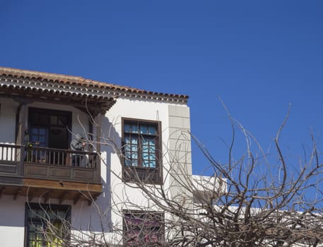 Wooden balcony typical on traditional house in colonial style in Canary islands, Tenerife with bare tree branches and blue sky background