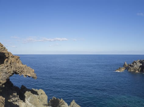 sea horizon with sharp rocks and cliffs in forward, creal blue sky background