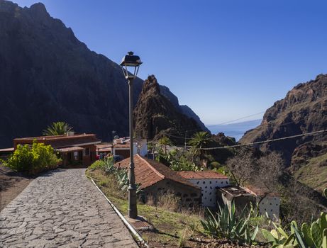 Canary Island, Tenerife  view on pitoresque Masca village with old stone houses, street lamp, cacti, beatiful green sharp hills, cliff, sea horizon and blue sky background