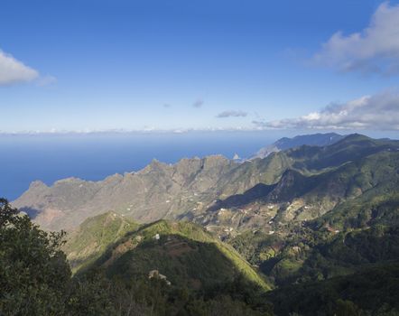 view point Amogoje, green hills with rock in the sea El Draguillo in anaga mountain, tenerife  canary island spain with dramatic blue sky white clouds background