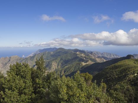 view point Amogoje, green hills with rock in the sea El Draguillo in anaga mountain, tenerife  canary island spain with dramatic blue sky white clouds background