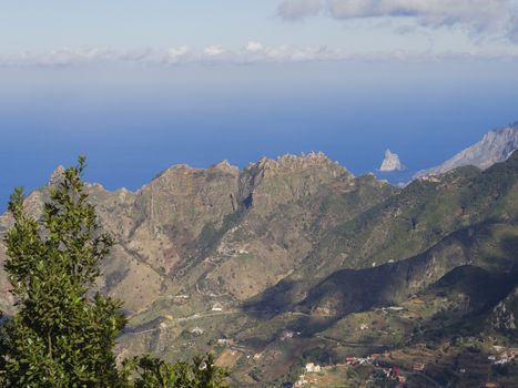 view point Amogoje, green hills with rock in the sea El Draguillo in anaga mountain, tenerife  canary island spain with dramatic blue sky white clouds background