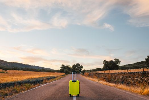 yellow suitcase on a road in the field